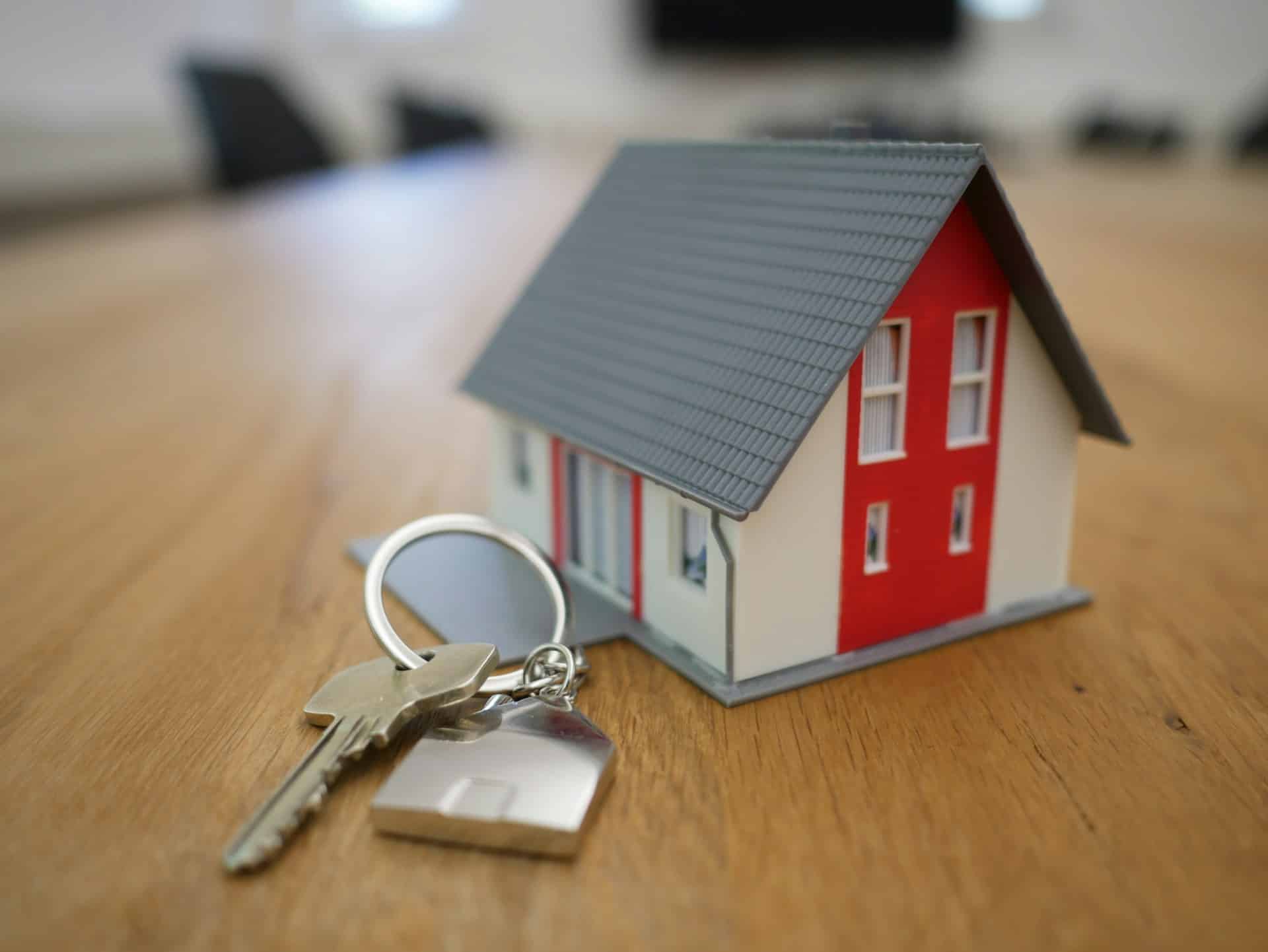 Miniature house model next to a set of silver keys on a wooden surface, symbolising property ownership and home registration